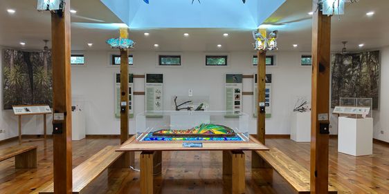 Inside the Discovery Centre, a timber strip floor and white walls. In the centre of the room is a wooden table with a stained glass sculpture in the centre. On wooden pillars are sculptures of flying animals made of stained glass and metal